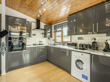 A kitchen with grey cabinets a washing machine a gas stove and wooden ceiling at Lakeview Lodge in South Lakeland Leisure Village