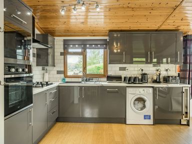 A kitchen with grey cabinets a wooden ceiling and floor a washing machine and kitchen appliances at Lakeview Lodge South Lakeland Leisure Village