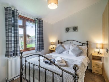 A bedroom with a double metal bed two bedside tables with lamps and a window with curtains at Lakeview Lodge in South Lakeland Leisure Village