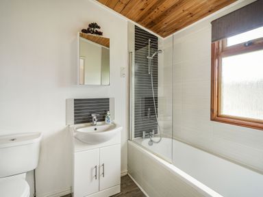 A bathroom with a toilet sink cabinet shower over bathtub and window at Lakeview Lodge in South Lakeland Leisure Village