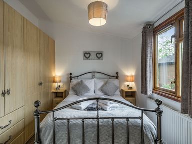 A bedroom with a metal frame bed two bedside tables with lamps a window wooden wardrobe and folded towels on the bed at Lakeview Lodge in South Lakeland Leisure Village