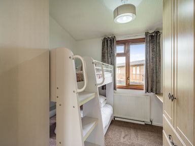 A small bedroom with a bunk bed window with curtains radiator and a wardrobe at Lakeview Lodge South Lakeland Leisure Village