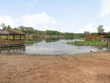 A lakeside view with a wooden gazebo on the left and wooden cabins along the shore at Lakeview Lodge in South Lakeland Leisure Village