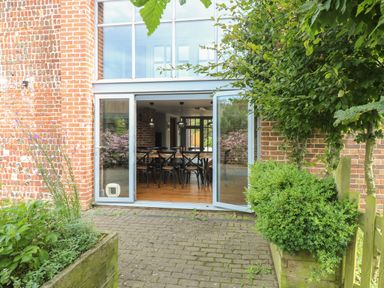 A patio with plants and wooden fence opening to a dining area with wooden table and chairs at The Barn in Tunstead near Hoveton & Wroxham