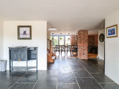 An open room with slate tile floor a black console table on the left and a dining area with black chairs and brick walls at The Barn in Tunstead near Hoveton & Wroxham