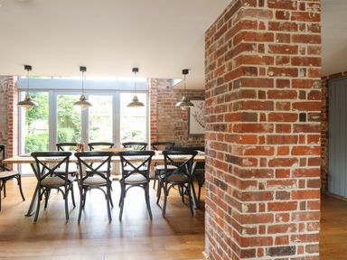 A dining area with a wooden table and black chairs near glass doors and brick walls at The Barn in Tunstead near Hoveton & Wroxham