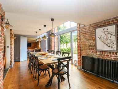 A dining room with a long wooden table surrounded by black chairs and pendant lights at The Barn Tunstead near Hoveton & Wroxham