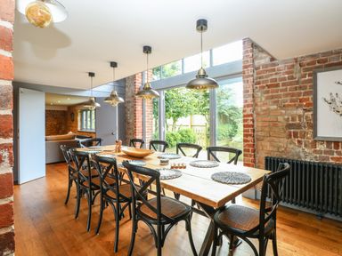 A dining room with a wooden table and black chairs near large glass windows and brick walls at The Barn in Tunstead near Hoveton & Wroxham