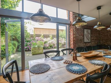 A dining area with a wooden table and black chairs next to large glass sliding doors showing an outside garden at The Barn in Tunstead near Hoveton & Wroxham