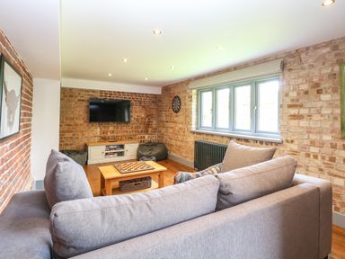 A living room with a grey sofa a wooden coffee table a wall mounted television and exposed brick walls at The Barn in Tunstead near Hoveton & Wroxham