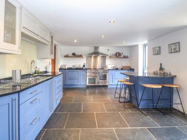 A kitchen with blue cabinets a stainless steel oven stools and black countertops at The Barn Tunstead near Hoveton and Wroxham
