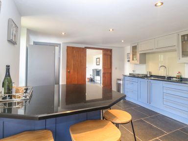 A kitchen with blue cabinets black countertop wooden stools and a refrigerator at The Barn Tunstead near Hoveton & Wroxham