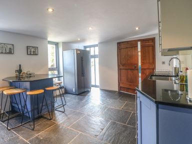 A kitchen with a blue island and wooden stools next to a refrigerator and wooden door at The Barn in Tunstead near Hoveton & Wroxham