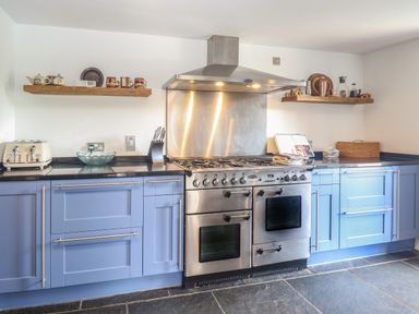 A kitchen with blue cabinets a stainless steel oven stove with hood and wooden shelves with kitchenware at The Barn in Tunstead near Hoveton & Wroxham