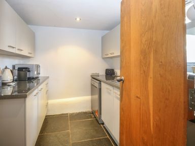 A small kitchen with white cabinets a kettle a coffee machine a dishwasher and a wooden door at The Barn in Tunstead near Hoveton & Wroxham