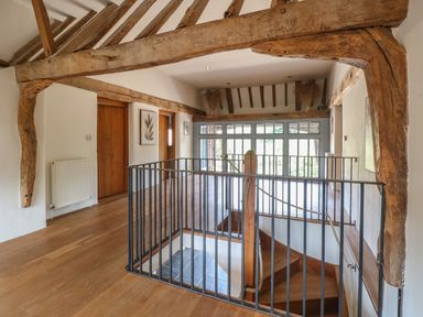 An upstairs hallway with wooden beams a staircase with black metal railing and wooden doors at The Barn Tunstead near Hoveton & Wroxham