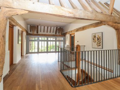 An upper floor hallway with wooden beams wooden floor a staircase with black metal railing and large windows at The Barn Tunstead near Hoveton & Wroxham