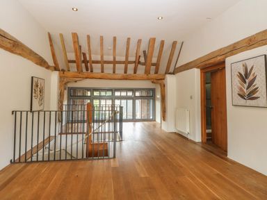 An upstairs hallway with wooden beams on the ceiling wooden floors metal railings and framed leaf artwork at The Barn in Tunstead near Hoveton & Wroxham