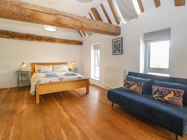 A bedroom with a wooden bed and side tables with lamps and a blue sofa with patterned pillows at The Barn in Tunstead near Hoveton & Wroxham