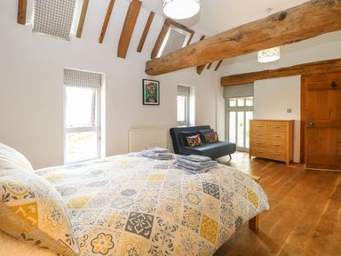 A bedroom with a bed a sofa a chest of drawers wooden beams and windows at The Barn in Tunstead near Hoveton & Wroxham