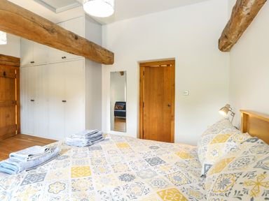A bedroom with a bed covered by patterned bedding towels on the bed wooden beams on the ceiling a wooden door and white built-in wardrobes with a mirror on the wall at The Barn Tunstead near Hoveton & Wroxham