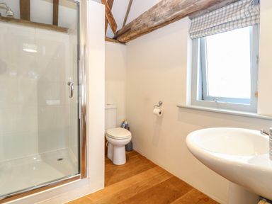A bathroom with a shower enclosure toilet sink wooden floor and a window at The Barn Tunstead near Hoveton & Wroxham
