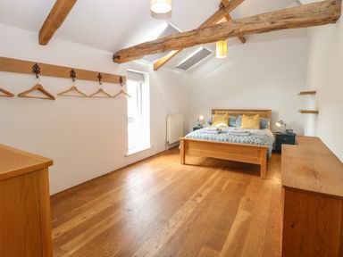 A bedroom with a wooden bed, nightstands, hanging hooks with hangers, and exposed ceiling beams at The Barn Tunstead near Hoveton & Wroxham