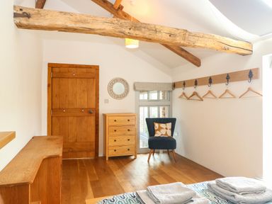 A bedroom with wooden door chest of drawers chair and wooden coat rack with hangers at The Barn Tunstead near Hoveton & Wroxham
