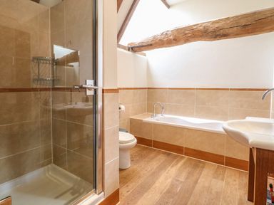 A bathroom with a shower cubicle toilet bathtub and sink with wooden flooring at The Barn in Tunstead near Hoveton & Wroxham