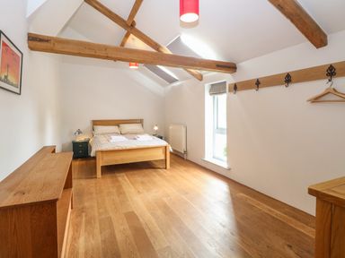 A bedroom with a wooden bed frame bedside tables wooden beams and a window at The Barn Tunstead near Hoveton & Wroxham