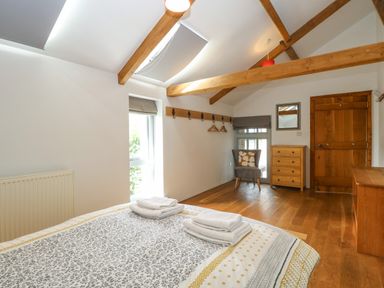 A bedroom with a bed and folded towels wooden beams a chair a small dresser wooden door and window blinds at The Barn in Tunstead near Hoveton & Wroxham