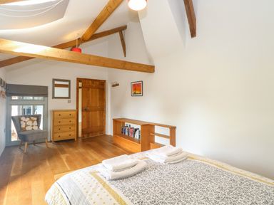 A bedroom with wooden beams a bed with towels a chair a chest of drawers and a bookshelf at The Barn in Tunstead near Hoveton & Wroxham
