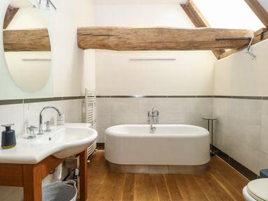 A bathroom with a bathtub a sink with a mirror a wooden ceiling beam and wooden floor at The Barn in Tunstead near Hoveton & Wroxham