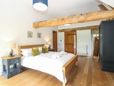 A bedroom with a wooden bed two green pillows wooden nightstands lamps wooden beams and a wardrobe at The Barn in Tunstead near Hoveton & Wroxham