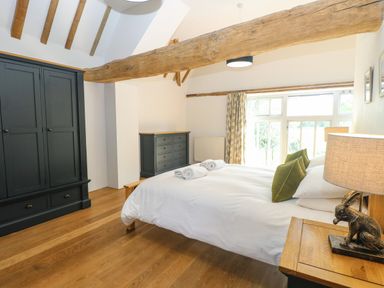 A bedroom with wooden beams a bed with white linens green pillows towels and dark furniture at The Barn Tunstead near Hoveton & Wroxham