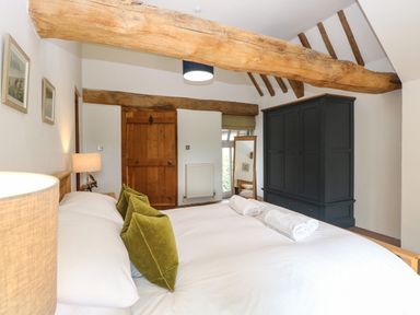 A bedroom with a bed with green cushions and towels beside a wooden door and a dark wardrobe at The Barn in Tunstead near Hoveton & Wroxham