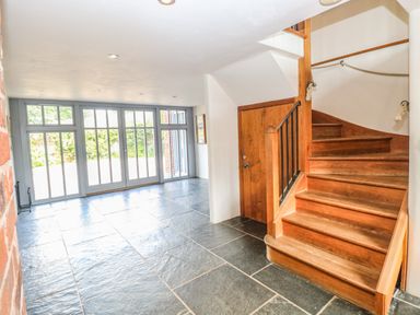 A hallway with slate tile flooring wooden staircase and a wall of glass doors at The Barn in Tunstead near Hoveton & Wroxham