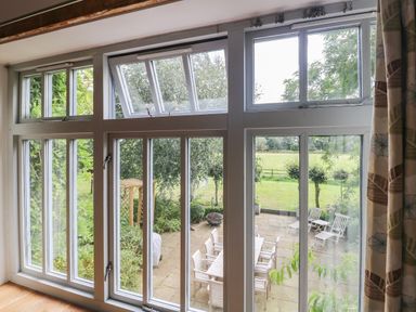 A large window looking out onto a patio with outdoor furniture and garden at The Barn in Tunstead near Hoveton & Wroxham