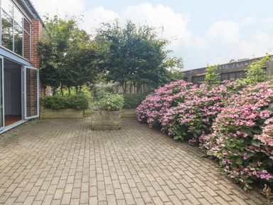 A paved patio area with flower beds and shrubs along a wooden fence at The Barn Tunstead near Hoveton & Wroxham