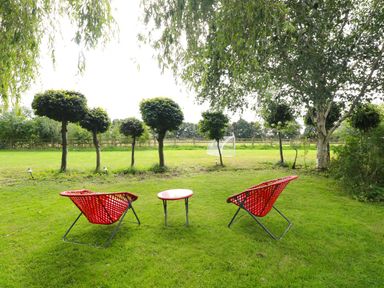 A garden with two red chairs and a small round table on grass near trimmed trees and a soccer goal at The Barn Tunstead near Hoveton & Wroxham