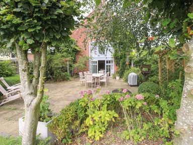 An outdoor patio with a dining table and chairs surrounded by trees and shrubs at The Barn in Tunstead near Hoveton & Wroxham