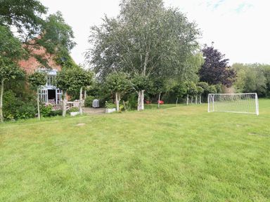 A grassy backyard with a small soccer goal trees and outdoor furniture near a brick house at The Barn in Tunstead near Hoveton & Wroxham