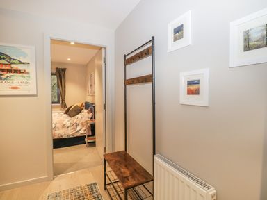 A hallway with a wooden and metal coat rack a radiator and framed pictures on the wall leading to a bedroom at River View in Backbarrow