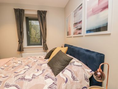 A bedroom with a bed with pillows and patterned bedding near a window with curtains at River View in Backbarrow
