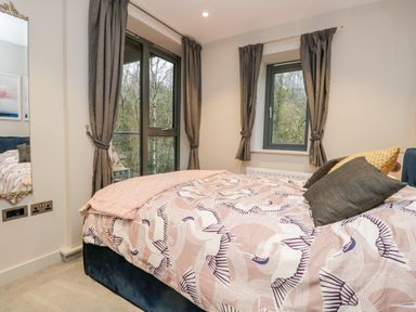 A bedroom with a bed with patterned bedding and windows with gray curtains at River View in Backbarrow
