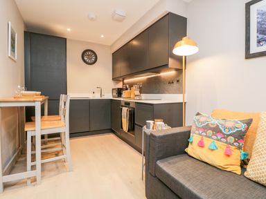 A kitchen area with black cabinets a dining table with two chairs and a sofa with colorful cushions at River View in Backbarrow