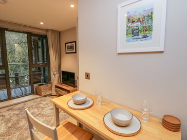 A dining area with a table set for two next to a living room with a television and balcony at River View in Backbarrow
