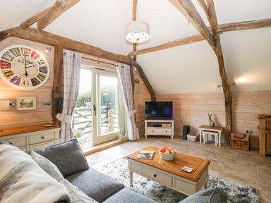 A living room with a gray sofa a wooden coffee table a wall clock and a television at The Barn at Rapps Cottage Rapps near Ilminster