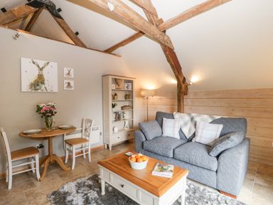 A living room with a gray sofa a wooden coffee table a small dining table with two chairs and a bookshelf at The Barn at Rapps Cottage in Rapps near Ilminster