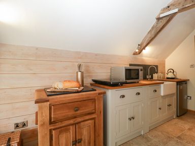 A kitchen counter with a loaf of bread on a cutting board and a microwave on cupboard at The Barn at Rapps Cottage Rapps near Ilminster